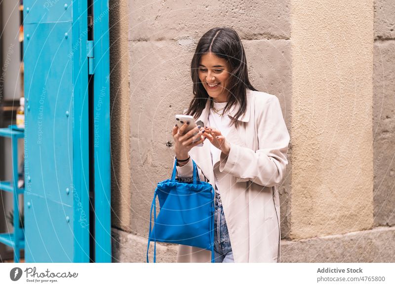 Cheerful woman browsing smartphone on street text message online internet city urban social media appearance female town lady attractive light style device