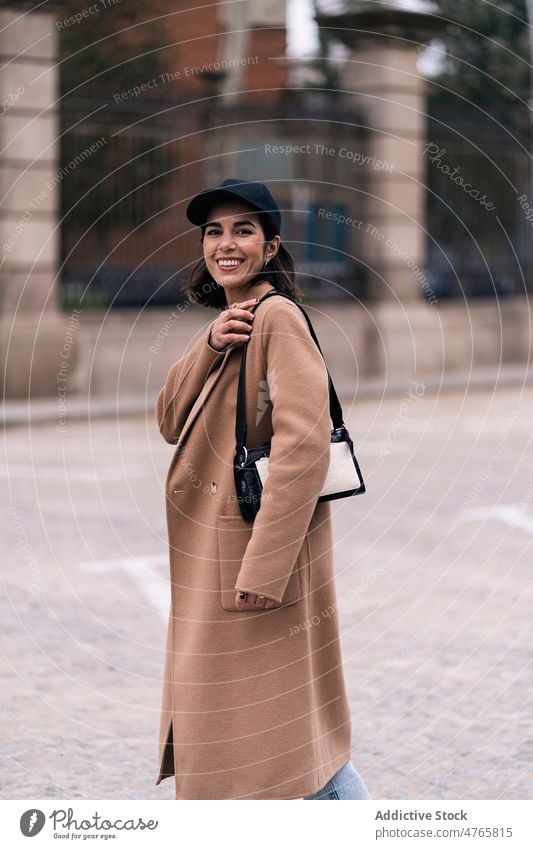 Positive woman in coat on street style city outfit trendy fashion urban appearance feminine female happy cheerful handbag cap glad headwear positive smile