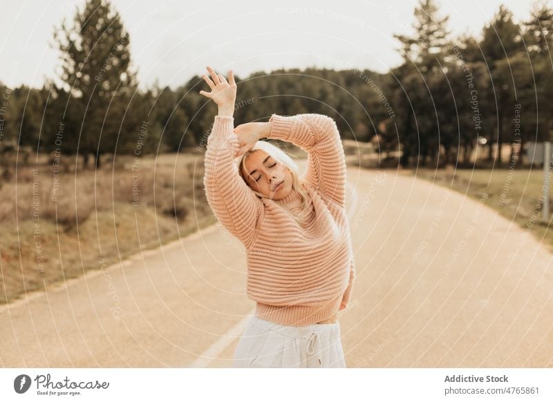 Blond woman enjoying dance in the road freedom nature eyes closed dream forest tree portrait serene spread arms style woods calm woodland sweater harmony