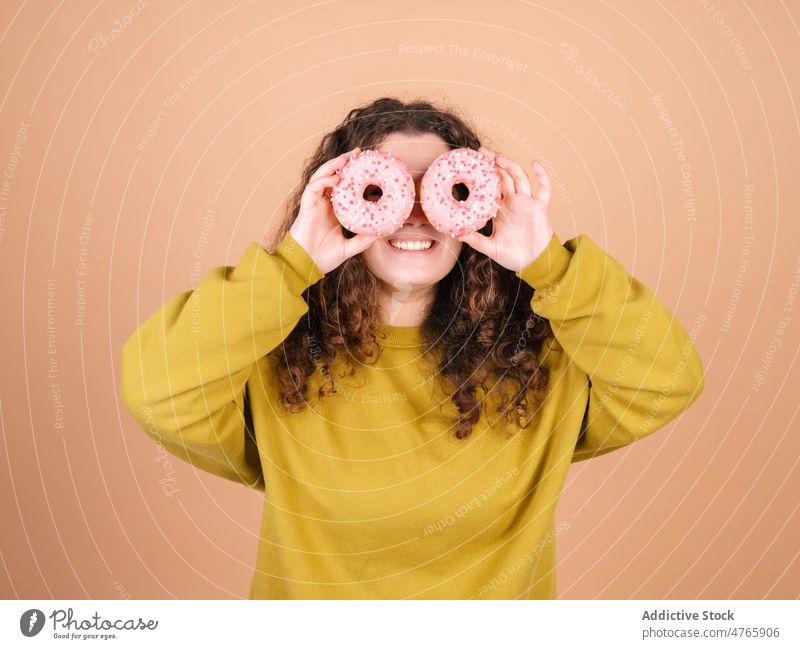 Cheerful woman covering eyes with sweet donuts in studio model glaze having fun happy pleasure sprinkle cover eyes cheerful female positive dessert hide face