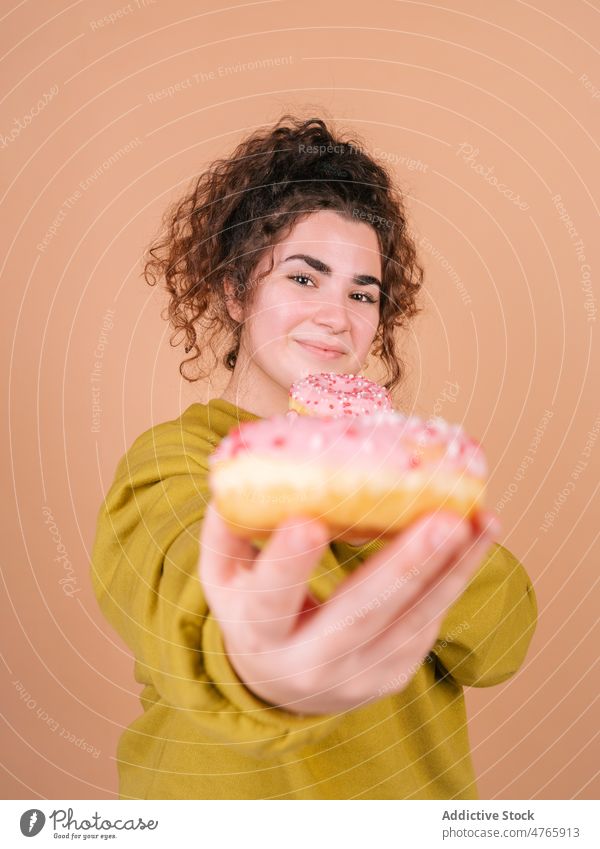 Happy woman eating sweet donuts and reaching to camera happy give dessert enjoy taste share female delicious icing treat hungry sugary glaze food bakery
