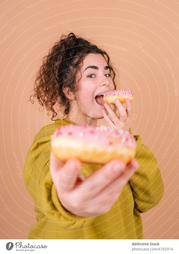 Happy woman eating sweet donuts and reaching to camera happy give dessert enjoy taste share female delicious icing treat hungry sugary glaze food bakery
