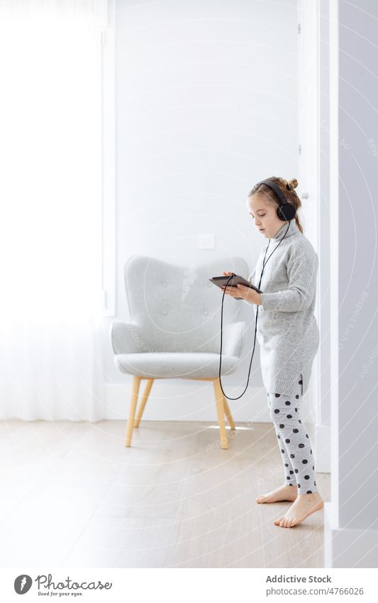 Happy girl using tablet and listening to music in headphones playlist digital addict free time depend device gaze gadget kid barefoot doorway pastime wire