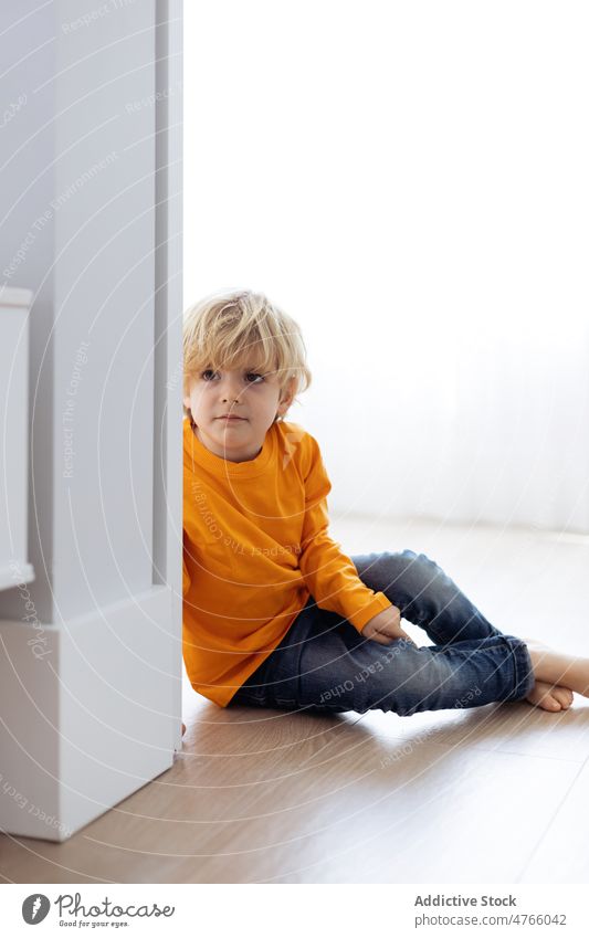Cute little boy sitting on parquet near wall kid childhood curious interest home apartment room cute explore legs crossed floor barefoot at home adorable blond