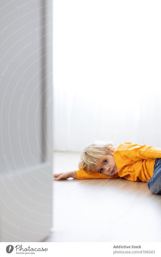 Cute little boy lying on parquet near wall kid childhood curious interest home apartment room cute explore floor at home adorable blond carefree serious modern