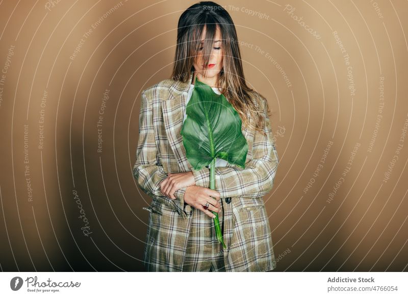 Stylish woman in checkered suit with fresh leaf of monstera model confident style formal classy female brunette makeup appearance serious plant personality