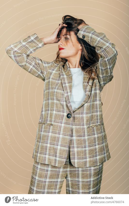 Stylish woman in suit ruffling hair in studio model style ruffle hair checkered touch hair trendy confident cool female fashion appearance contemporary