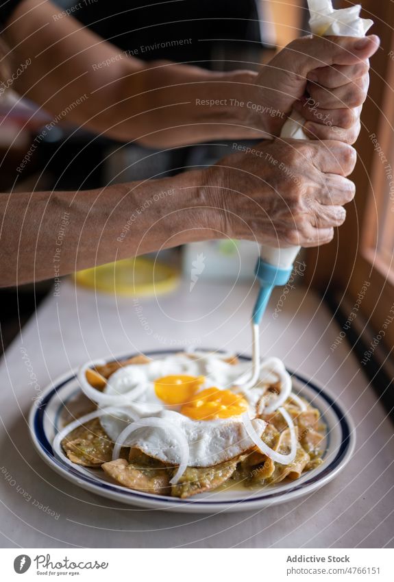 Anonymous person pouring sauce on dish with fried eggs and nachos cook culinary meal tortilla cuisine serve Mexican food mexican table kitchen delicious tasty