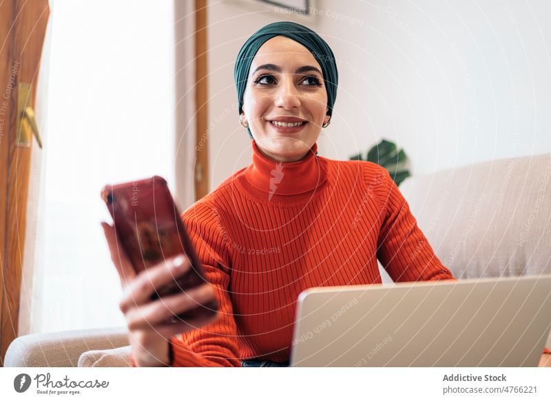 Muslim female using smartphone on sofa woman portrait laptop home rest social media muslim ethnic islam casual headscarf living room gadget couch browsing
