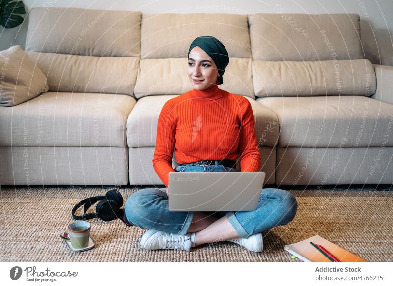 Female freelancer working on floor woman portrait muslim laptop using home ethnic headscarf typing islam telework sit project remote female casual mat tea data
