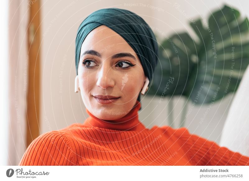 Muslim female listen music on sofa woman portrait muslim using earphones earbuds tws wireless home rest social media weekend ethnic islam playlist casual