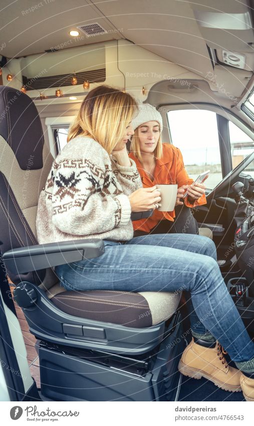 Women with a coffee looking mobile sitting in the front seat of a camper van women drinking winter woman morning open door motorhome friends sisters family