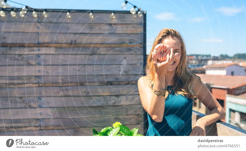 Funny woman posing covering her face with a doughnut funny young unrecognizable copy space goofing around smiling delicious laughing terrace rooftop sweet