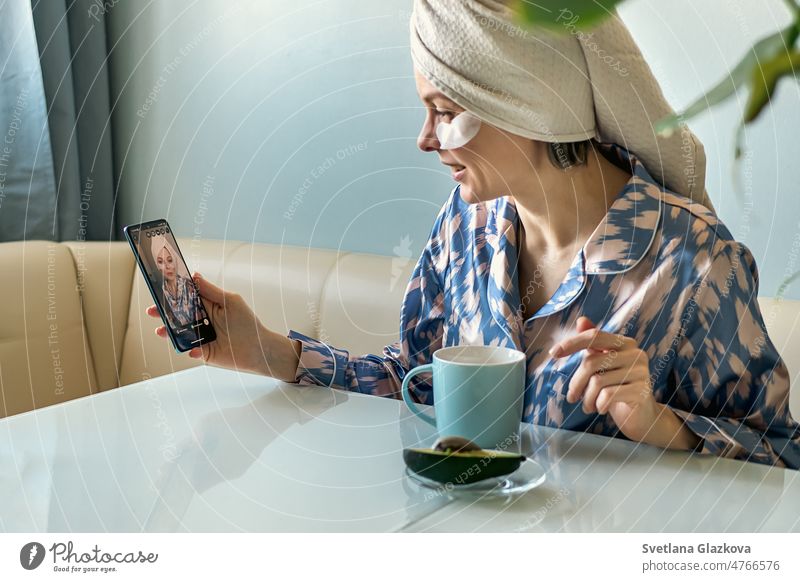 Morning routine. A woman in home clothes, pajamas and a towel drinks tea coffee at breakfast and talks on a mobile phone smartphone health care nutrient