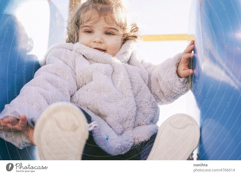 Little girl enjoying a sunny winter day at the playground playful baby toddler park slide curly spanish european adorable lovely childhood babyhood fun funny