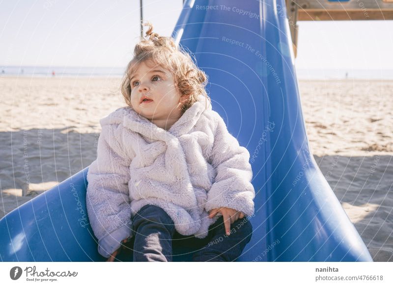 Little girl enjoying a sunny winter day at the playground playful baby toddler park slide curly spanish european adorable lovely childhood babyhood fun funny