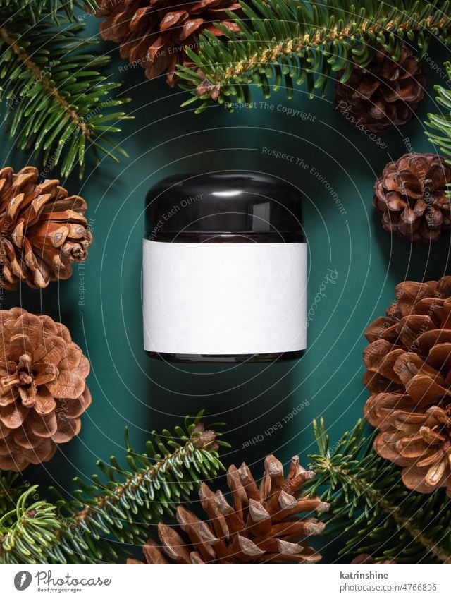 Brown glass jar near fir branches and pine cones on dark green top view. Brand packaging mockup. One pump skincare cream serum Healthcare natural cosmetics spa