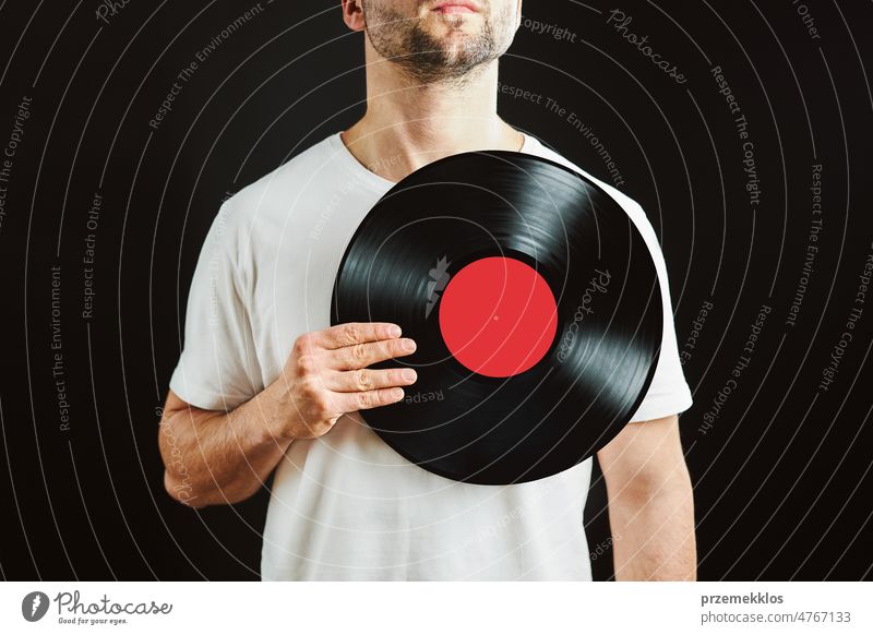 Man holding vinyl record over heart. Music passion. Vintage music style. Male holding old vinyl disk standing on black background. Retro music vintage disc