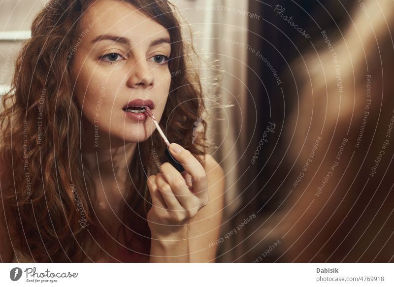Woman applying make up in front of mirror woman lipstick makeup beauty self curly portrait face cometic model mouth lipcare skin gloss beautiful female people