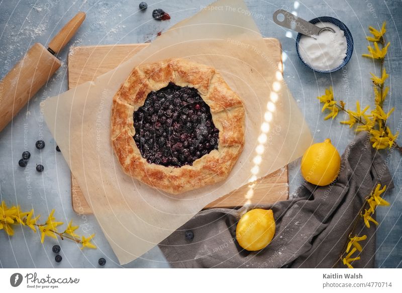Rustic blueberry and lemon tart with fresh yellow flowers and light gray background. food baked goods baking pastry fruit cooking dessert home-made
