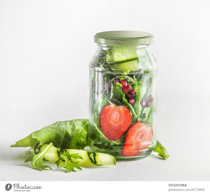 Salad in glass jar with green salad leaves, strawberries, cucumber and pomegranate seeds. healthy food lunch to go vegetarian meal preparation front view snack