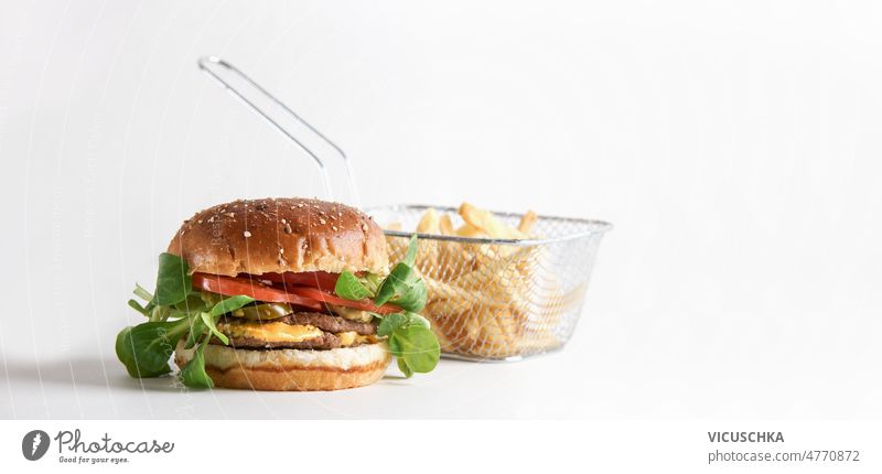 Hamburger with beef patty, lettuce, tomato, cheese, sauce and potato fries hamburger white background american food to go fast food metal basket front view bun