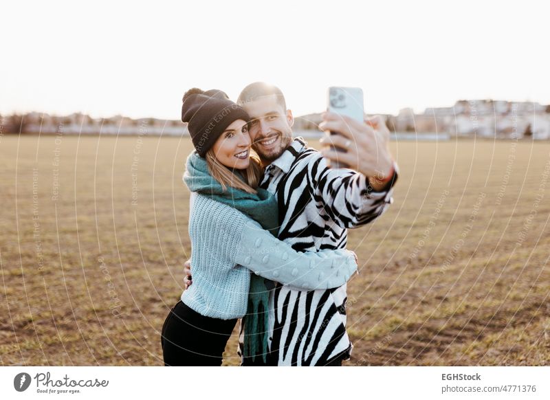 Couple taking a selfie photo with mobile phone in countryside at sunset happy together togetherness meadow romance romantic two affection dusk freedom joyful