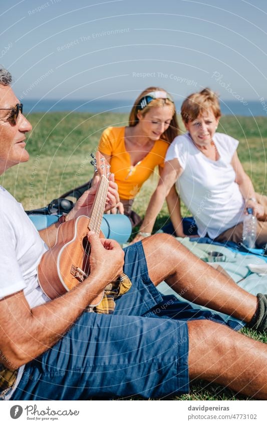 Senior man playing ukulele for his family sitting on a blanket during an excursion senior musical instrument outdoors adult together wife copy space daughter