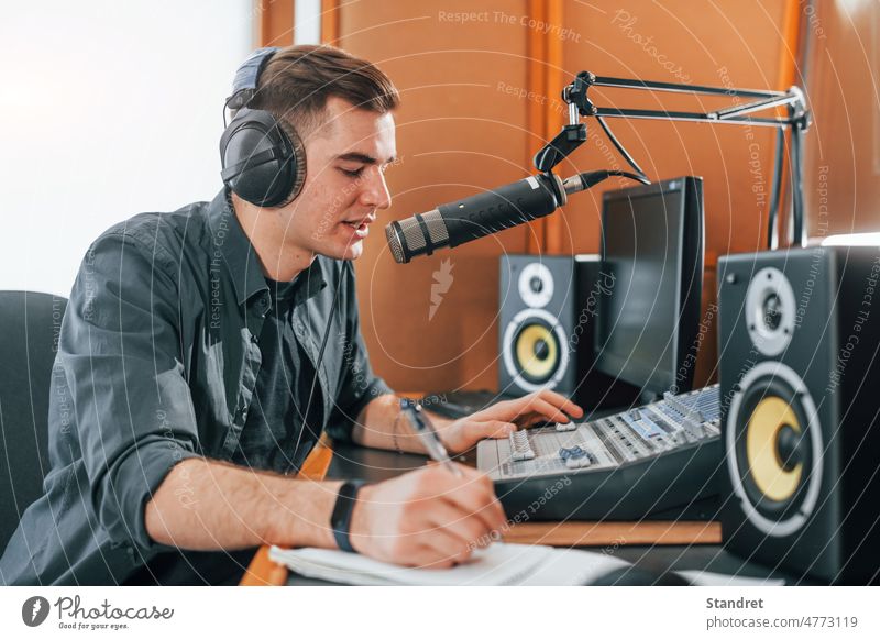 Talks and uses mic. Young man is indoors in the radio studio is busy by broadcast podcast interview show host presenter live recording air microphone journalist