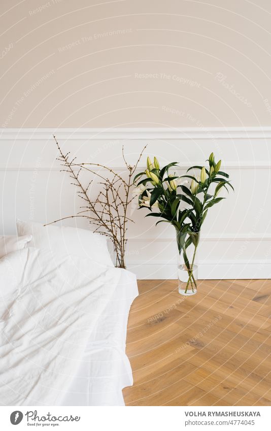 White lily flowers in a vase, tree branches in a vase near the bed. Details of the interior decor of the house apartment bedroom comfort comfortable cozy