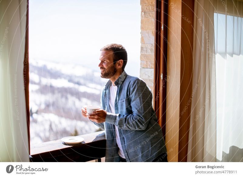 Young man with cup of hot tea at winter window apartment attractive beautiful beverage calm coffee cute drink enjoying face home hotel house interior indoors