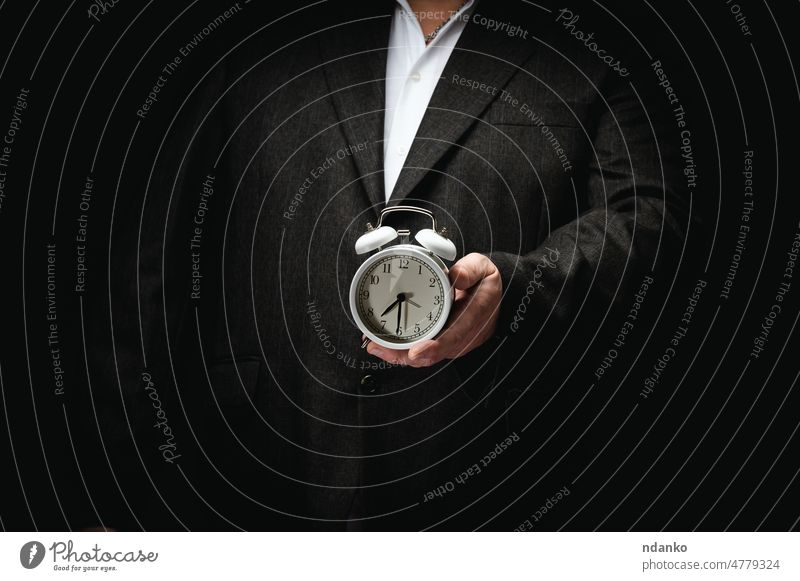 businessman in a suit holding a round alarm clock, half past seven in the morning. Clock change, early rise time concept watch hand hours deadline work minute