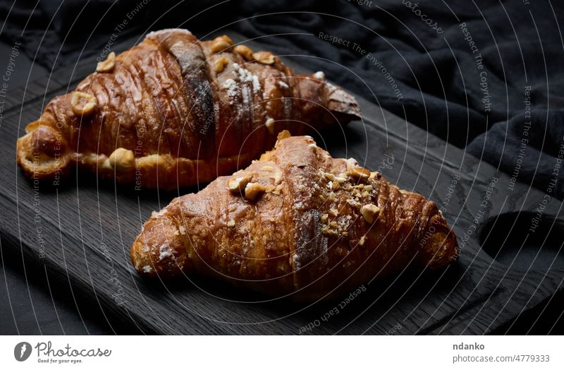 Baked croissants on a black wooden board sprinkled with powdered sugar, top view breakfast food bakery pastry bread brown baked fresh white french snack closeup