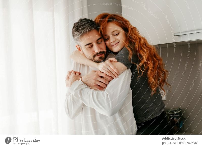 Loving couple hugging in kitchen relationship love bonding cuddle romantic affection redhead caress embrace eyes closed fondness together home spend time