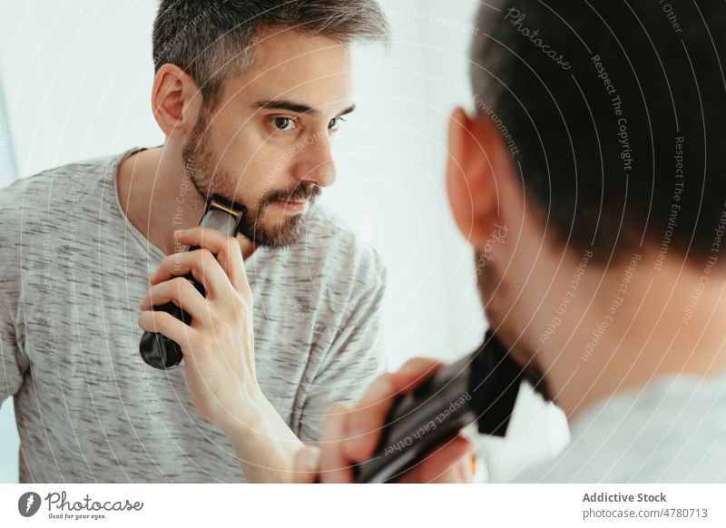 Man shaving beard with trimmer man shave routine unshaven mirror hygiene daily bathroom reflection home appearance male light guy everyday procedure treat