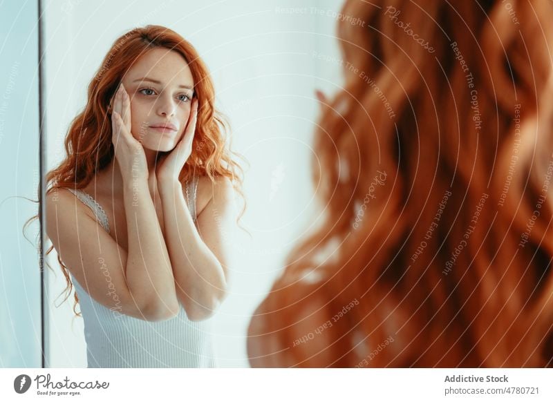 Woman touching face in bathroom woman mirror redhead hygiene routine reflection check daily everyday ginger skin care touch neck sink home morning long hair