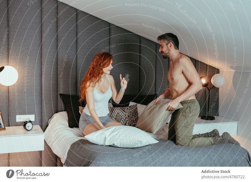 Cheerful couple fighting with pillows on bed bedroom red hair pillow fight having fun carefree relationship love bonding playful romantic affection fondness