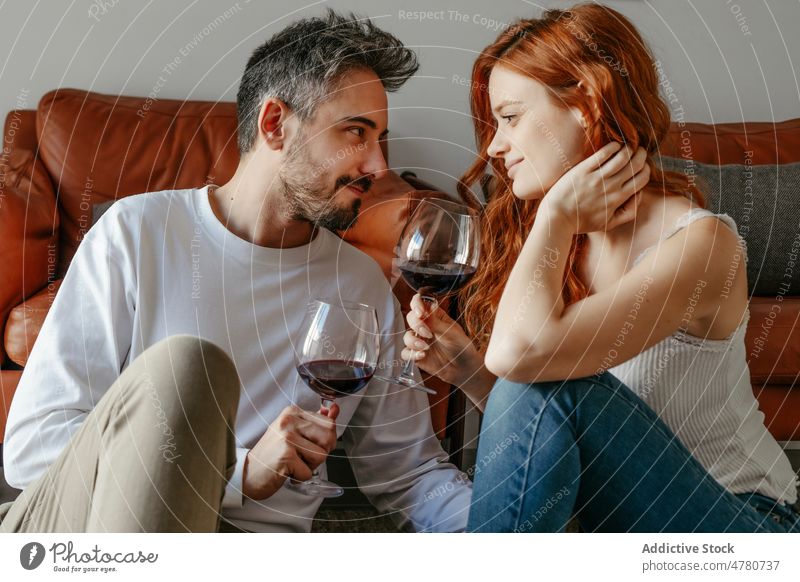 Loving couple with wineglasses on floor relationship love bonding romantic caress kiss celebrate affection redhead ginger alcohol booze together home spend time