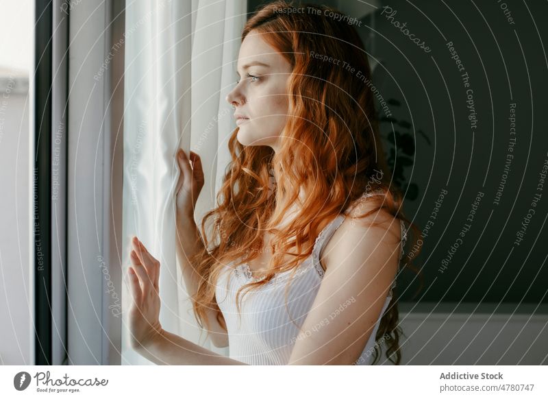 Sad redhead woman looking out window in room melancholy thoughtful dreamy sad lonely solitude pensive home tranquil curly hair domestic peaceful female mood