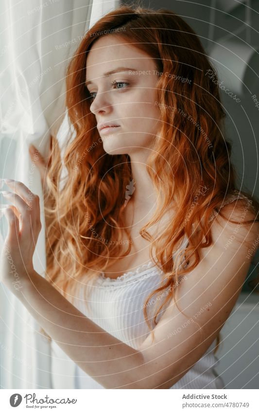 Sad redhead woman looking out window in room melancholy thoughtful dreamy sad lonely solitude pensive home tranquil curly hair domestic peaceful female mood