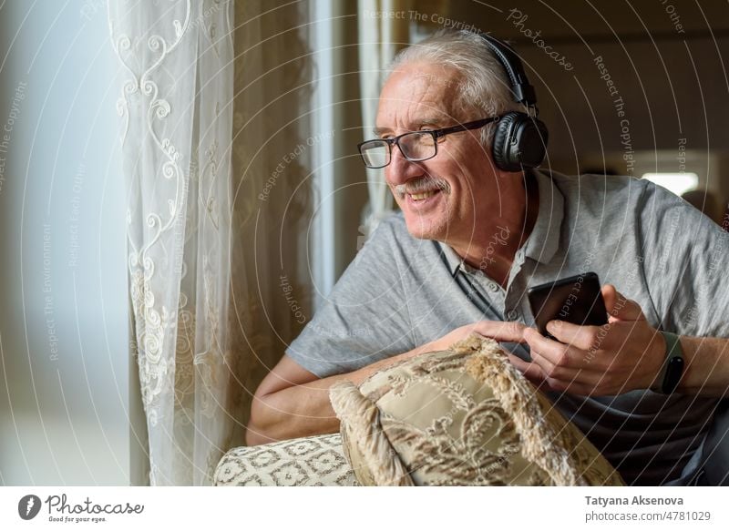 Senior man listening to music from phone person senior headphone mobile phone male enjoying technology lifestyle mature smartphone adult earphones online
