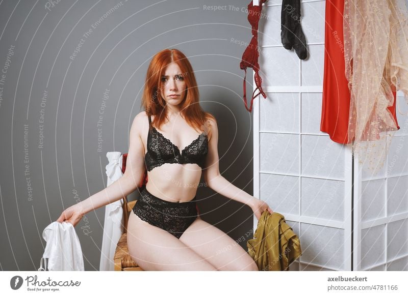 unhappy indecisive woman with many clothes has nothing to wear underwear outfit choice dress clothing undress folding screen change looking at camera lingerie