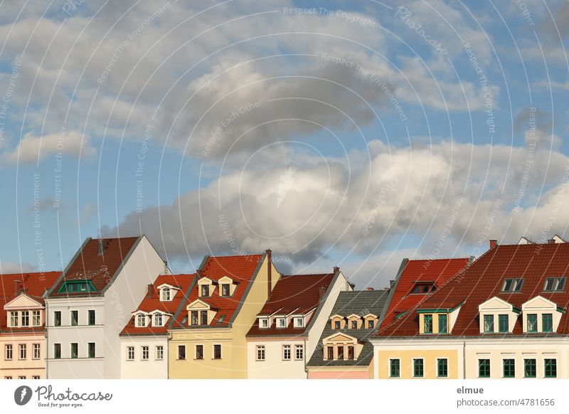 Partial view of a row of houses with apartment buildings of different size, color and construction and fair weather clouds / live / rent prices Housefront