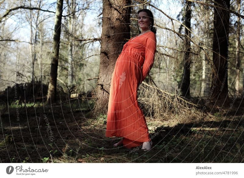 Young woman in red dress stands in spring forest and poses for camera Woman youthful pretty Long-haired Brunette daintily Beauty & Beauty 18 - 30 years