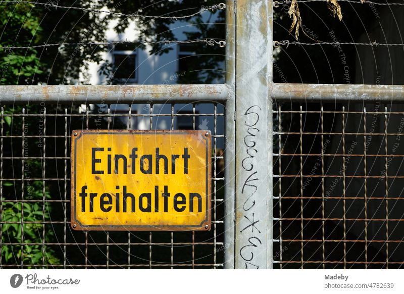 Rusty and yellowed yellow exit keep clear sign made of sheet metal with black writing on old wire fence of a yard gate in the east end of Frankfurt am Main in Hesse