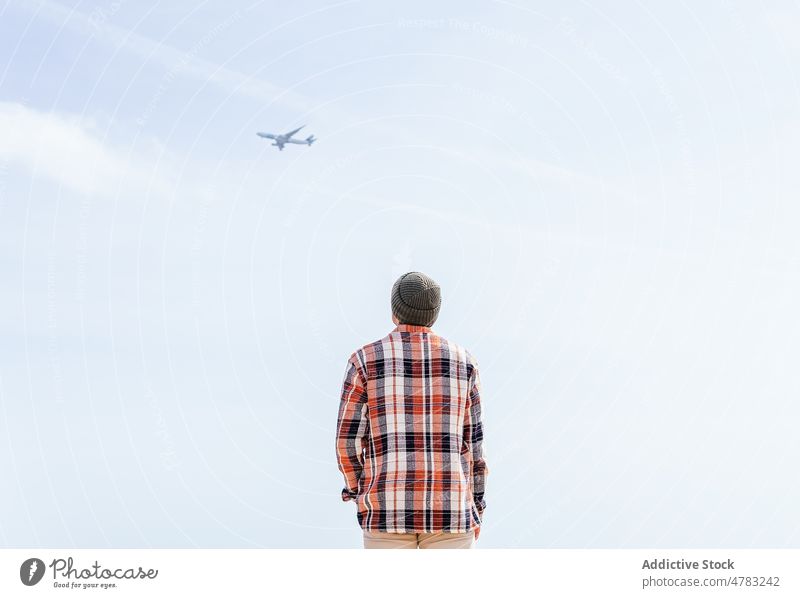 Unrecognizable man looking at airplane in sky observe flight blue sky aircraft admire contemplate aeroplane transport checkered shirt sunlight style scenic hat