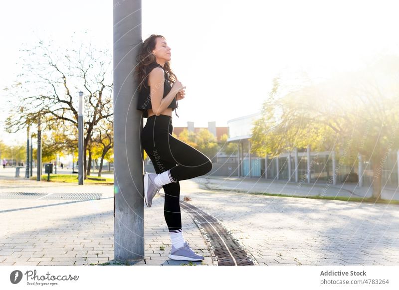 Sportive woman having break near post on street sportswoman athlete rest training workout pause city runner healthy lifestyle activewear sporty wellbeing