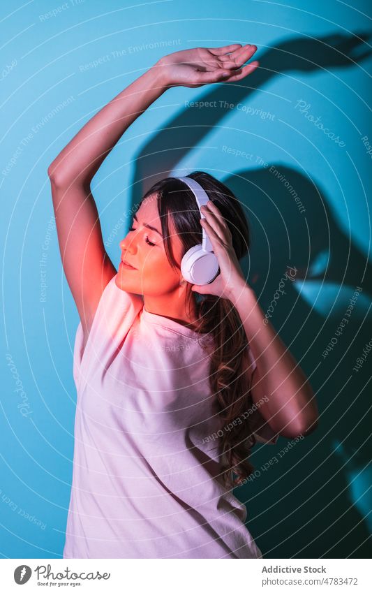 Woman listening to music in studio with lights woman headphones style red song raised arm meloman entertain hobby melody trendy colorful female sound vivid