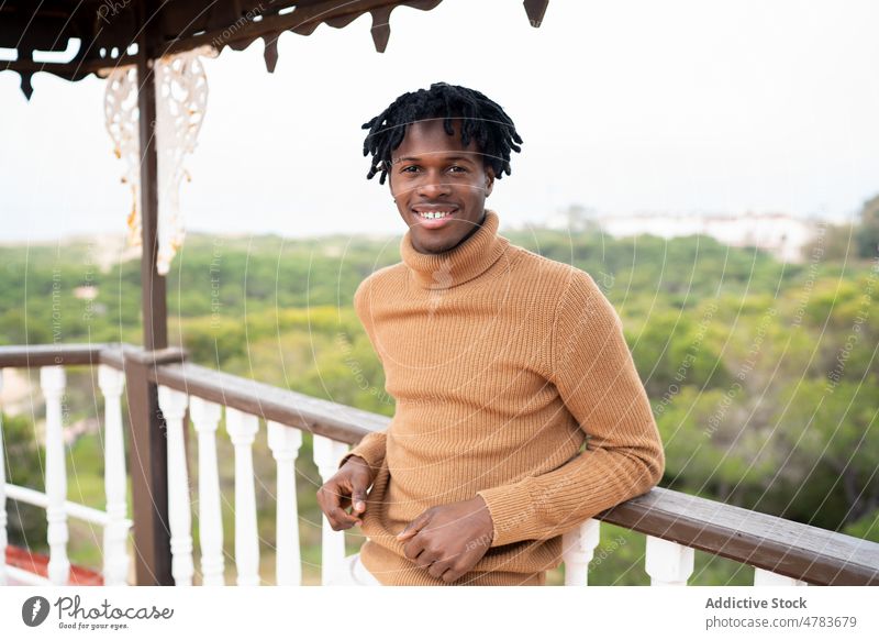 Happy black man with dreadlocks on terrace cheerful style appearance portrait outfit balcony turtleneck countryside fence rural happy wooden smile