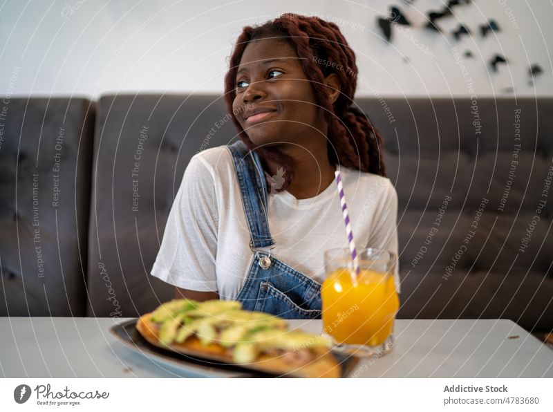 Black woman eating and drinking juice in cafe beverage straw orange smile happy glad refreshment thirst dish meal food female young black african american